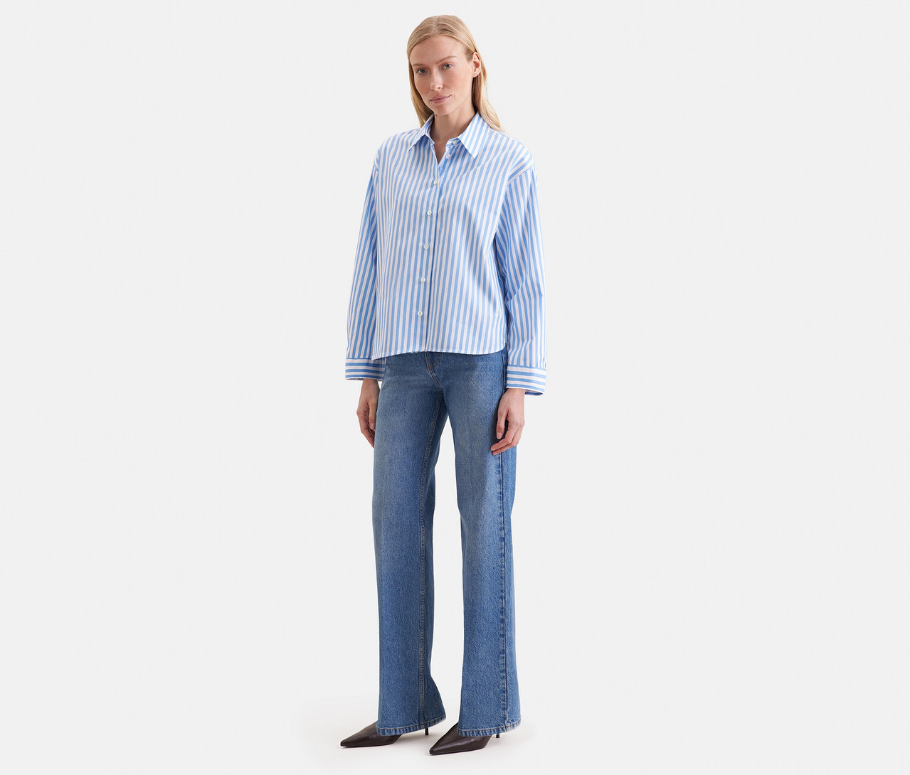 Eine Frau trägt eine blau-weiß gestreifte Seidensticker Oversize Hemdbluse und blaue Jeans.