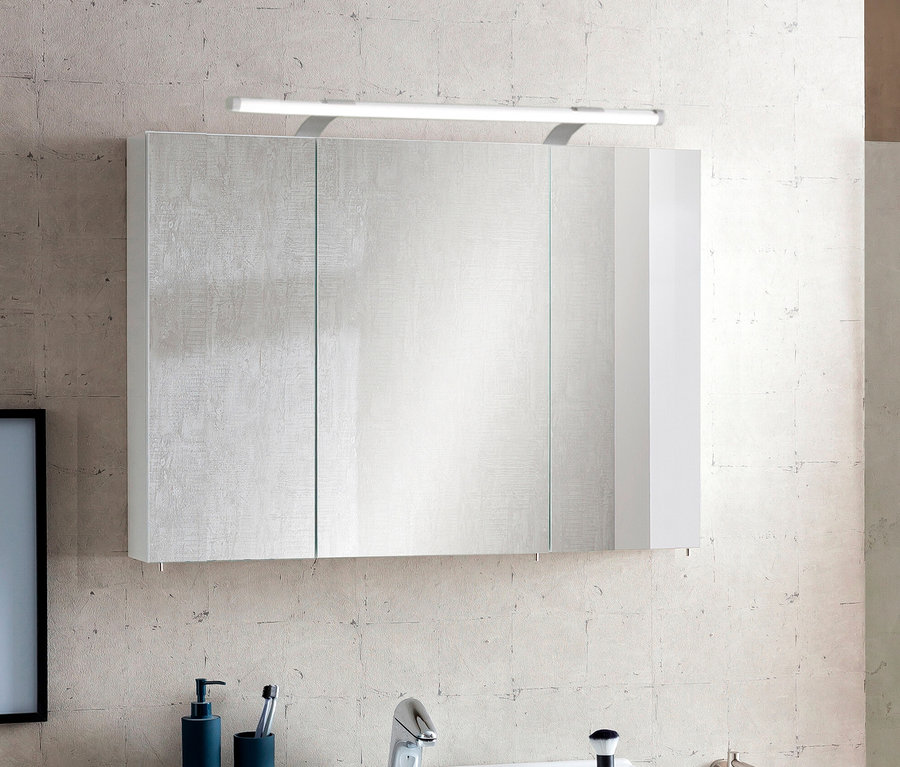 Spiegelschrank „Dorina“ mit Licht, 90 cm, an einer hellen, strukturierten Fliesenwand. Der Schrank hat Spiegeltüren und eine weiße Seitenwand. Darunter sind ein Waschbecken und blaue Badaccessoires teilweise sichtbar.