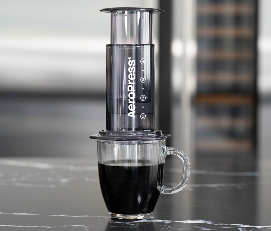 Ein schwarzer AeroPress Coffee Maker »Clear« steht auf einer Tasse mit Kaffee.