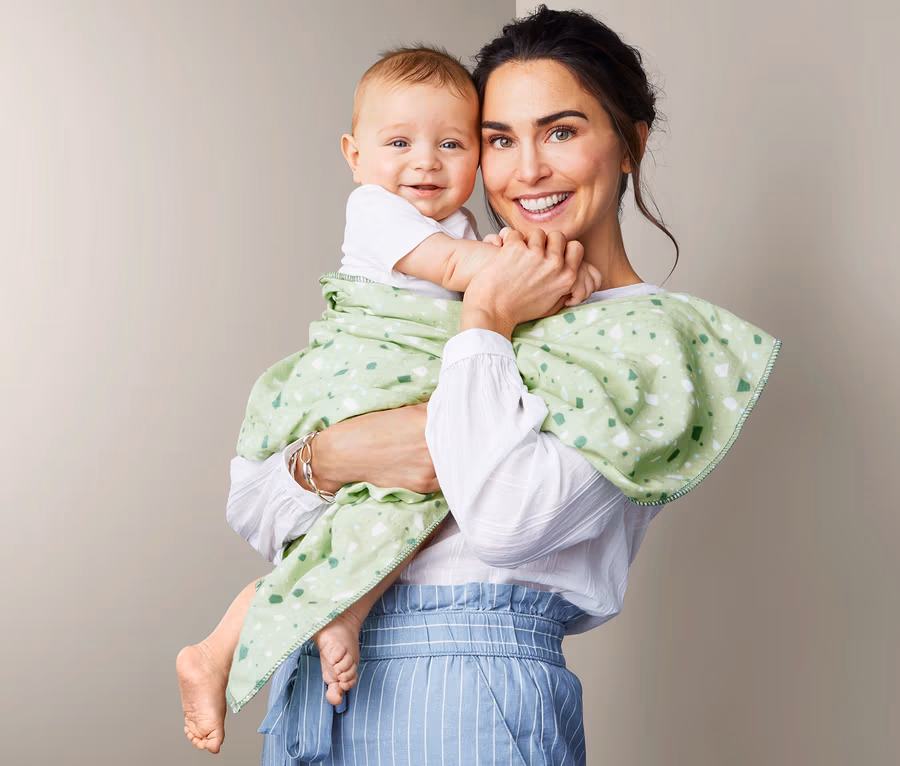 Frau hält ein Baby, das in eine Wohlfühldecke gewickelt ist.