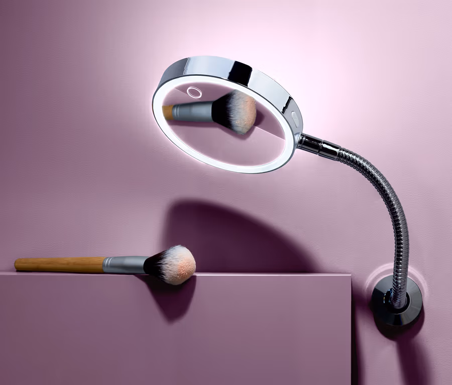Ein LED-Wandkosmetikspiegel und ein Make-up-Pinsel vor einem lila Hintergrund.