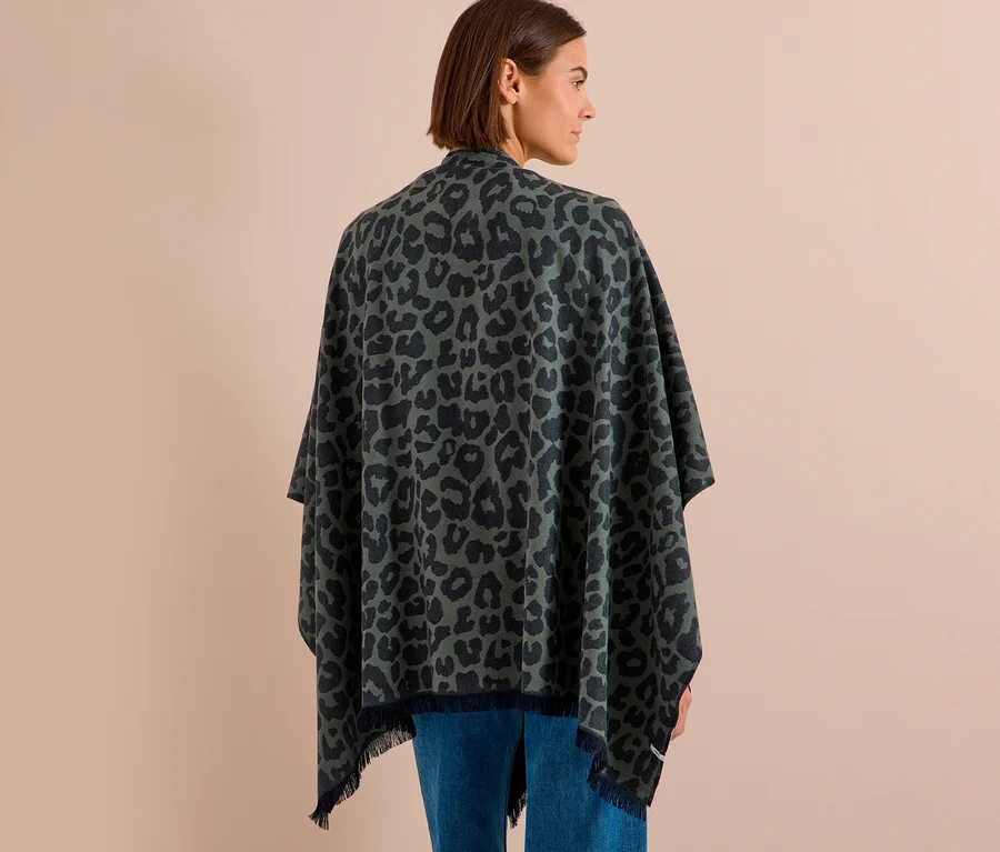 Frau von hinten in einem grün-schwarz gemusterten CECIL Poncho mit Leopardenmuster und Fransen über blauen Jeans.
