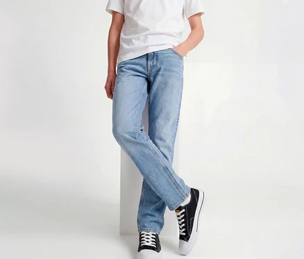 Person trägt ein weißes T-Shirt, hellblaue Jack&Jones JJOriginal Chris Jeans und schwarze Sneaker, lehnt mit gekreuzten Beinen an einem weißen Block.