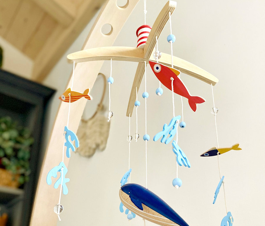 Ein Babymobile mit Holzfischen, Wal und Korallen hängt über einem Kinderbett. small foot Mobile mit Halterung »Seaside«.