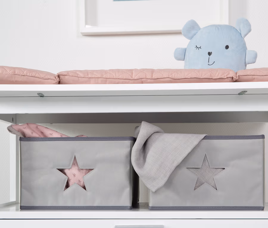 Weißer Wickeltisch mit rosa Auflage, blauem Teddybär und zwei grauen Aufbewahrungsboxen mit Sternen. Zu sehen ist die roba Wickelkommode »Hamburg« mit Wickelansatz.
