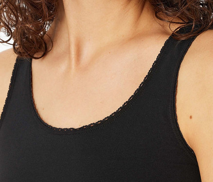 Detailaufnahme einer Frau mit braunem, gewelltem Haar, die ein schwarzes Tanktop mit Spitzenbesatz trägt.
