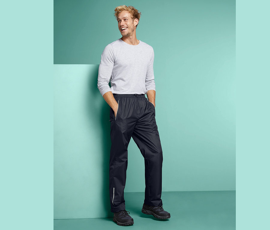 Mann steht mit Händen in den Taschen einer schwarzen Unisex-Regenhose.