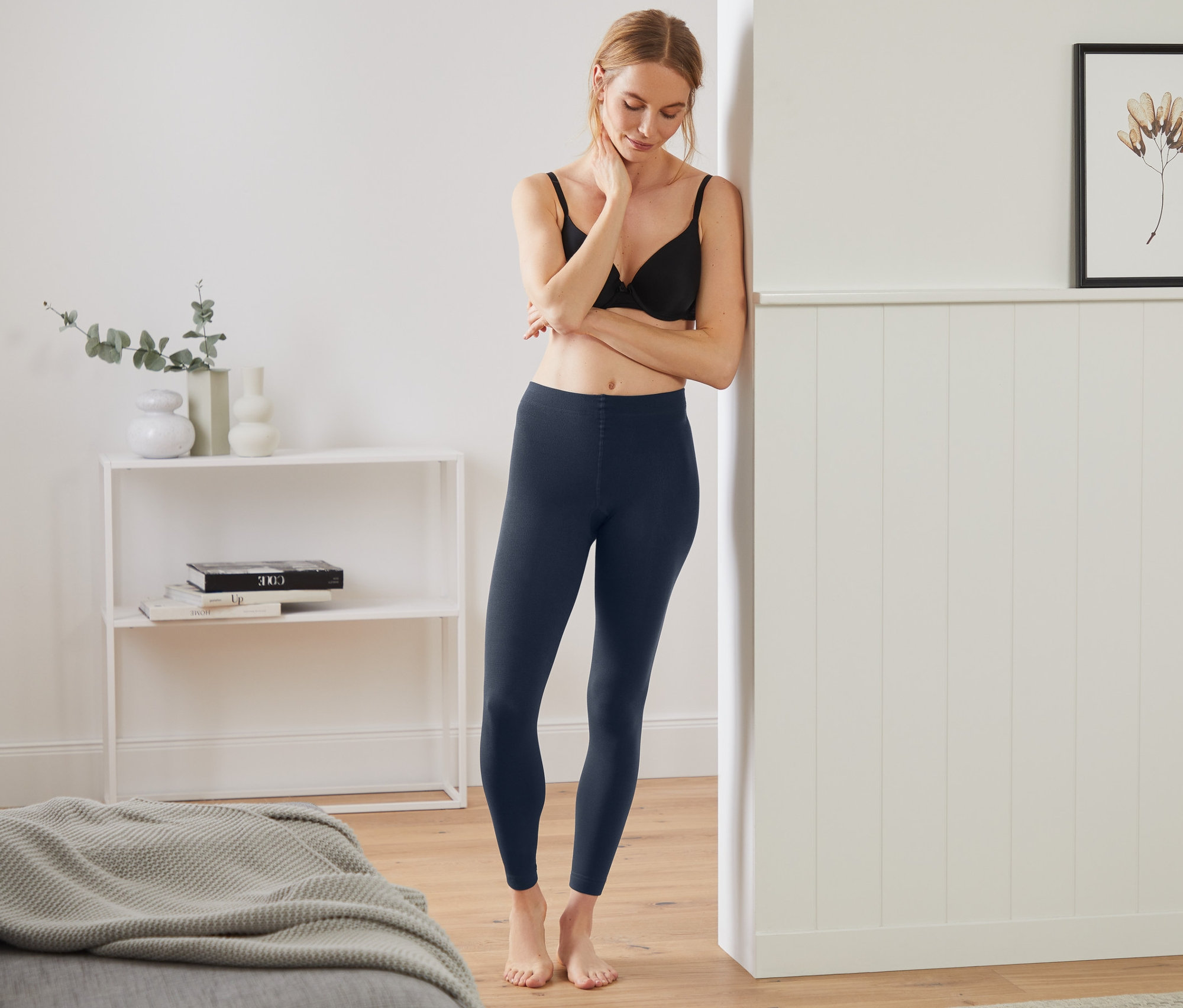 Eine Frau, die an eine Wand gelehnt ist, trägt Thermoleggings, blau und einen BH.