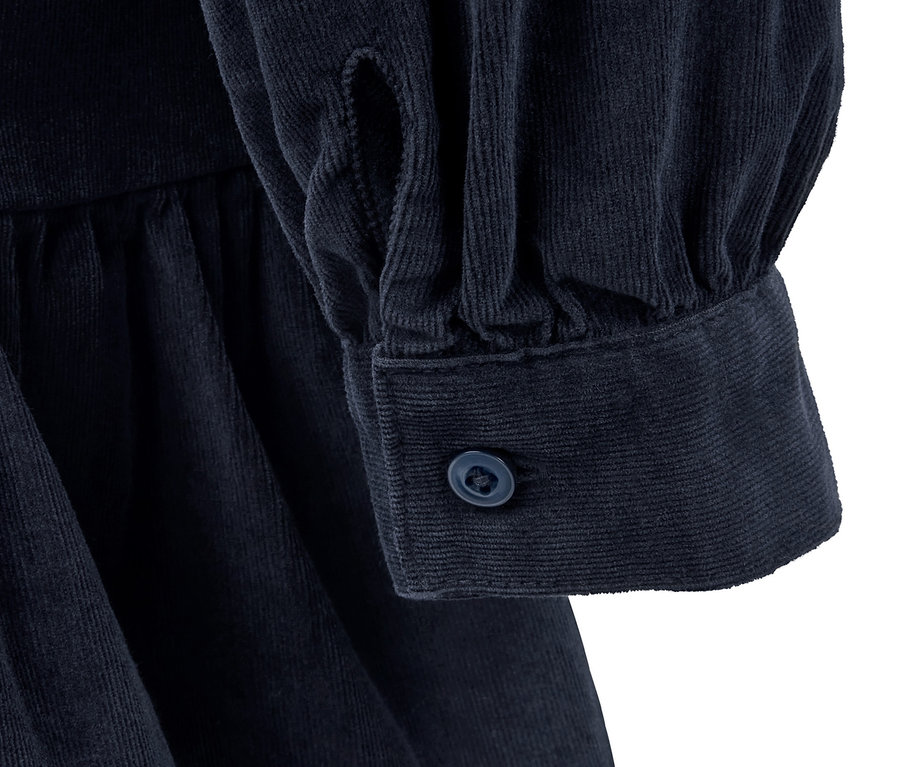Detailansicht eines Cordkleids mit langem Ärmel und Knopf.
