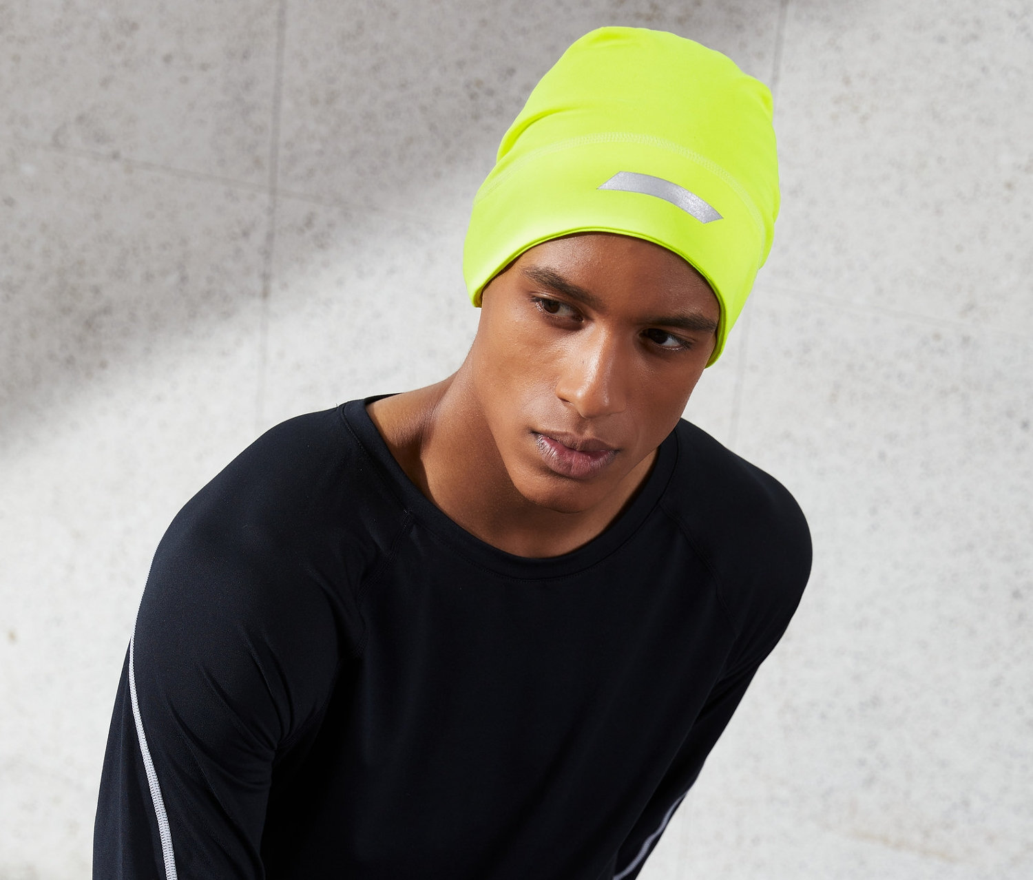 Mann trägt eine neongelbe Thermomütze mit Reflektorprint und schwarze Sportbekleidung.