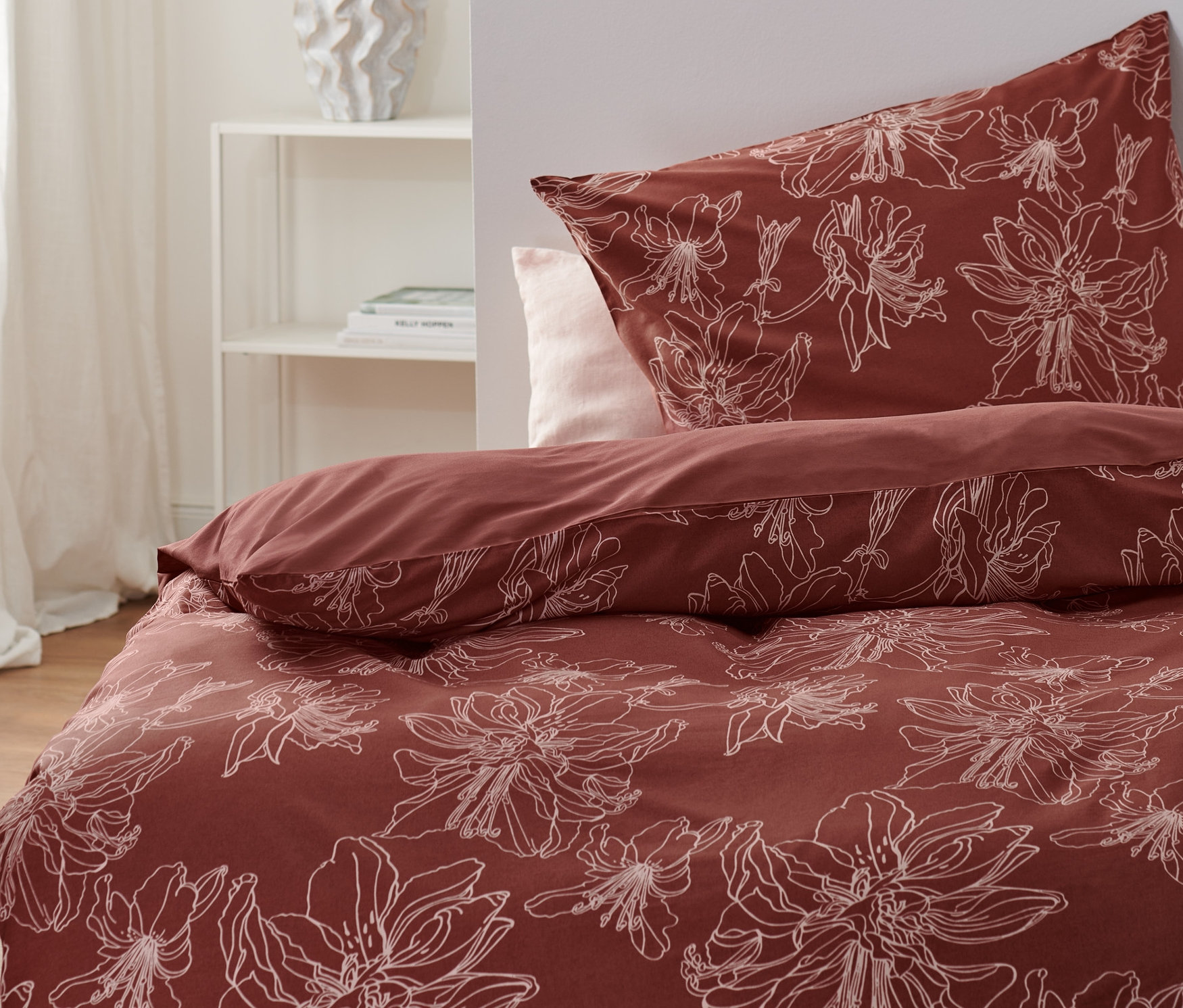 Geblümte Renforcé-Bettwäsche in Rot auf einem Bett, daneben ein weißer Nachttisch.