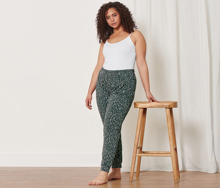 Frau im Hemdchen und Relaxhose lehnt an einem Holzhocker. Sie trägt auch 2 Hemdchen.