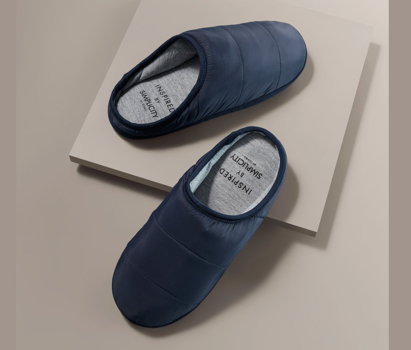 Zwei Stepp-Hausschuhe auf beigem Untergrund.