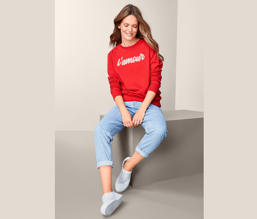 Frau sitzt und trägt ein rotes Sweatshirt mit Wording.