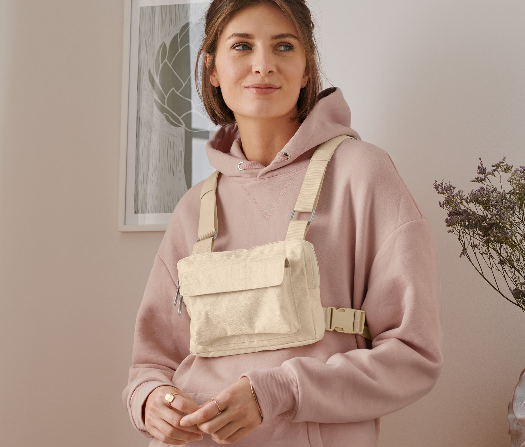 Frau trägt eine variable Umhängetasche in Beige und einen rosa Hoodie.