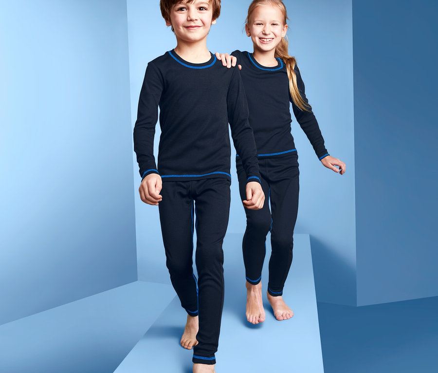 Ein Junge und ein Mädchen gehen barfuß auf einer blauen Oberfläche und tragen Funktionsunterwäsche.