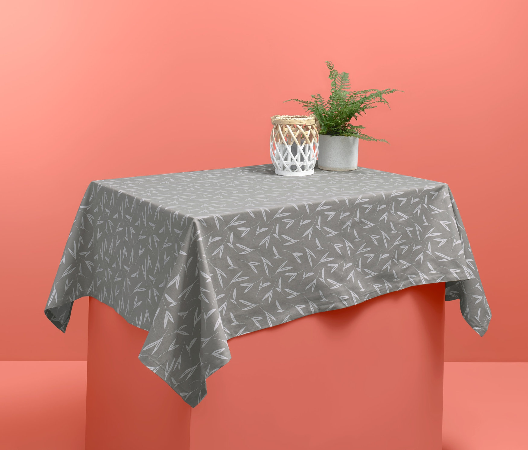 Graue Outdoor-Tischdecke mit weißem Muster auf einem Tisch. Auf der Tischdecke stehen eine dekorative Kerze und eine Topfpflanze.