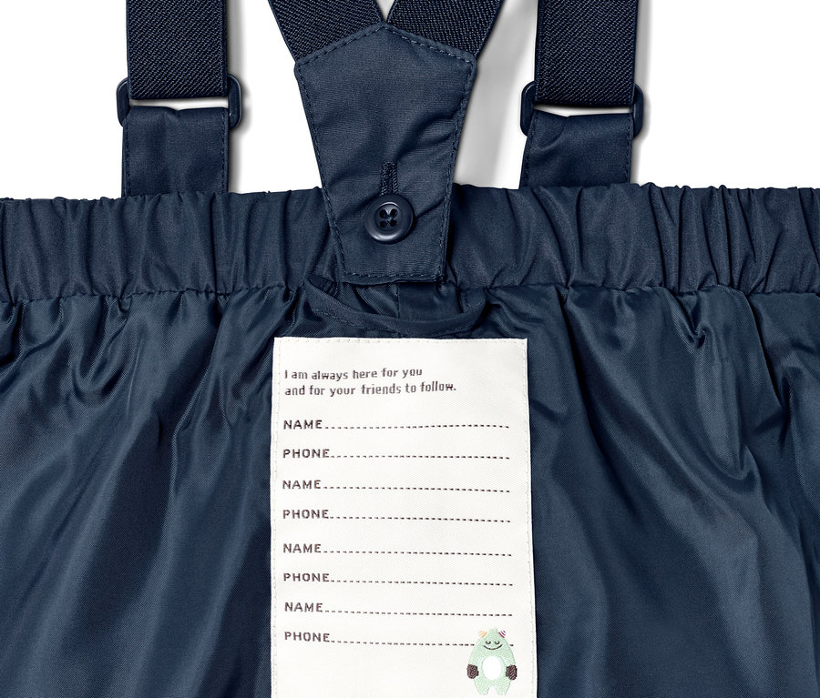 Detail einer blauen Regenhose mit Trägern und Namensschild.
