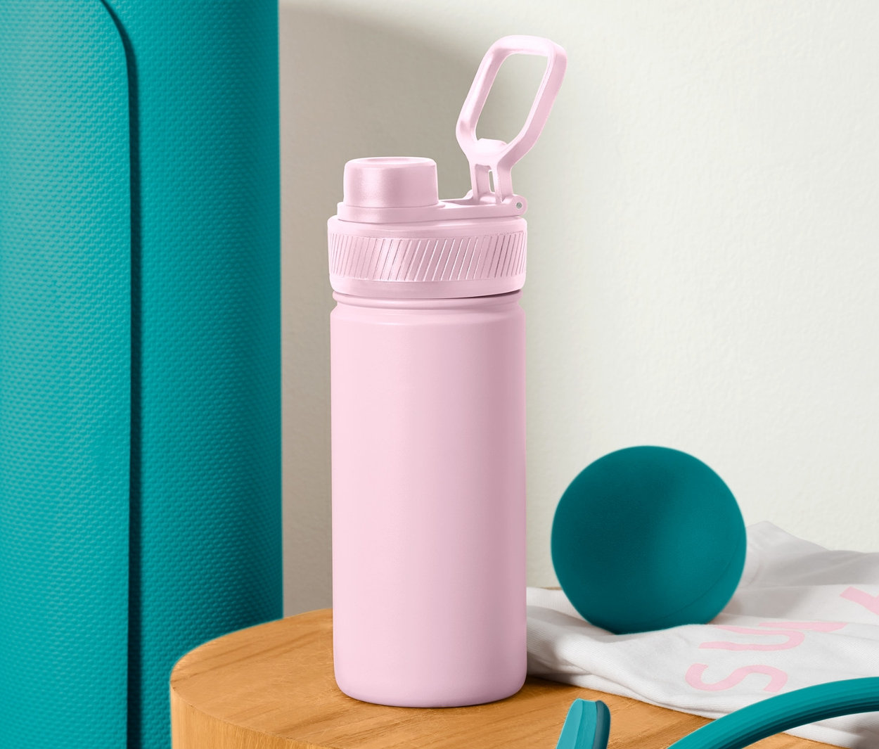 Eine grüne Yogamatte steht neben einer rosa Sport-Trinkflasche.