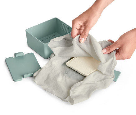 Hände wickeln Tofu in ein graues Tuch neben einer Tofupresse-und-bereiter ein.