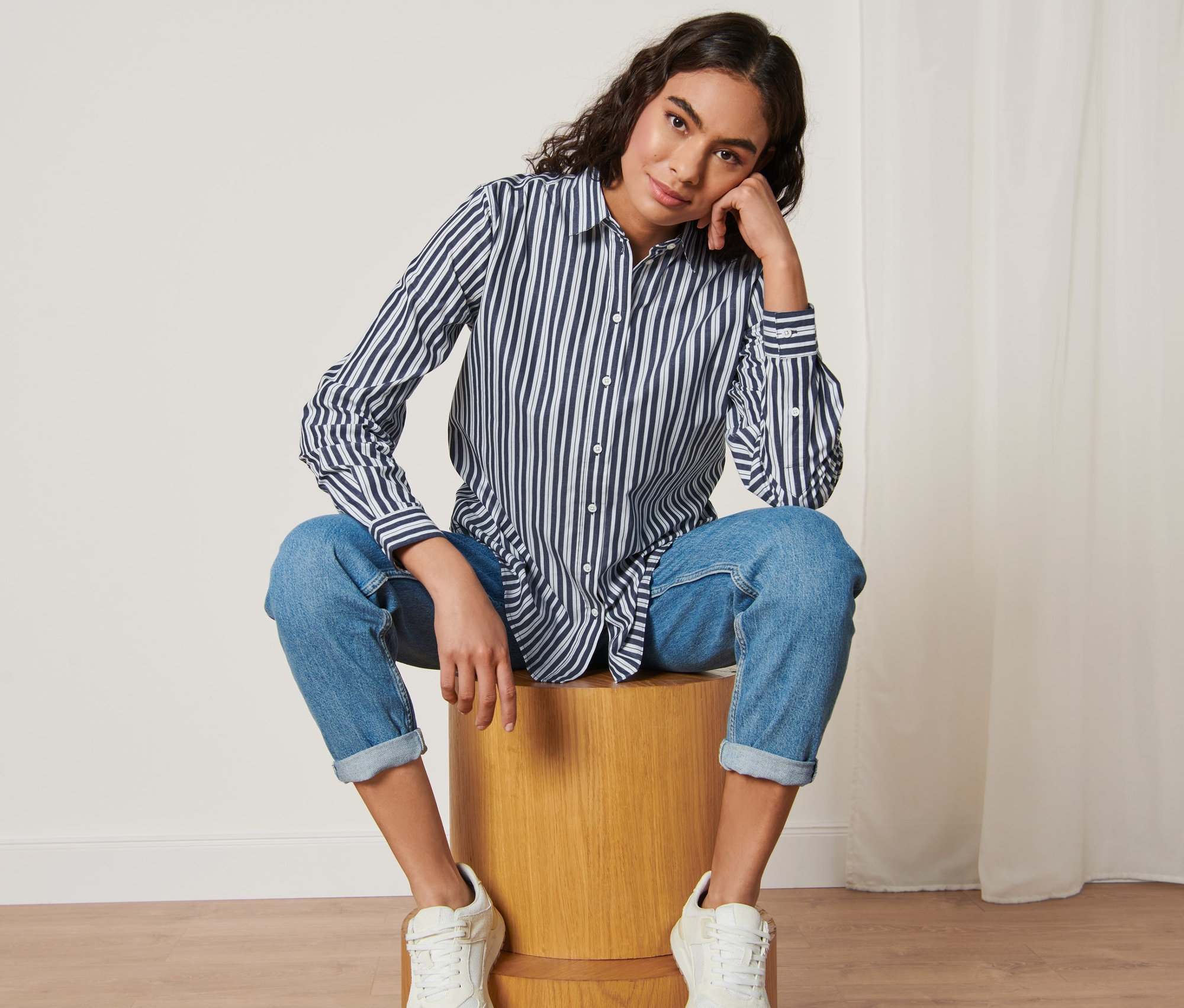 Frau sitzt auf einem Holzhocker und trägt eine Gestreifte Popeline-Bluse.
