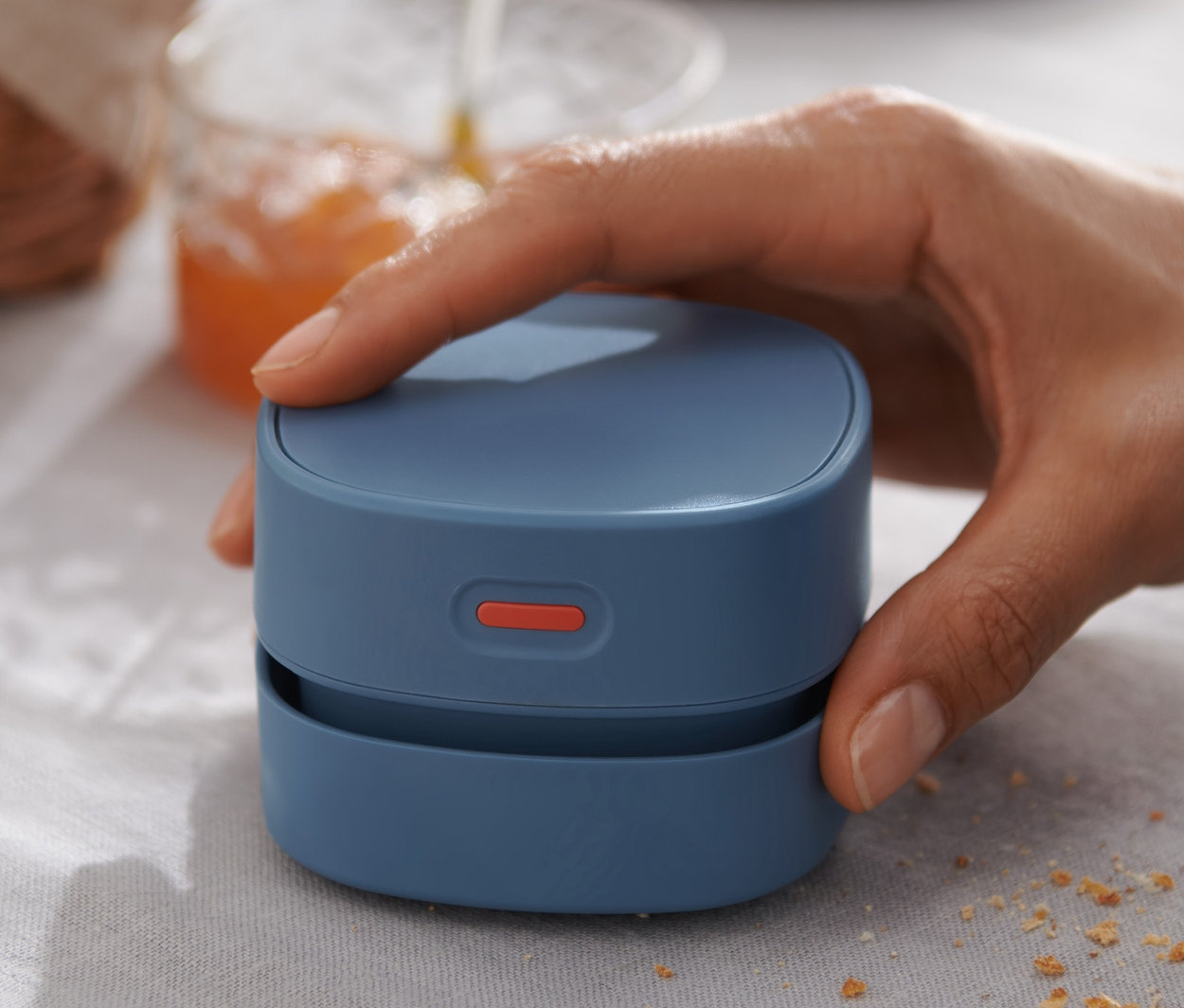 Hand hält Mini-Tischstaubsauger auf einem Tisch mit Krümeln.