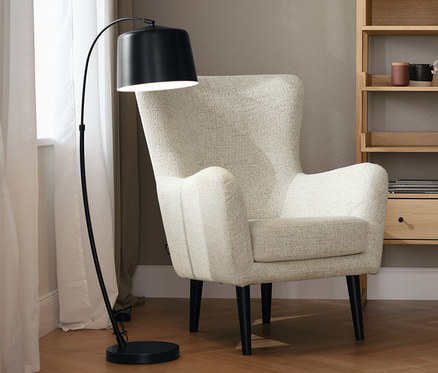 Beiger Sessel mit hoher Rückenlehne neben einem Regal aus Eichenholz und einer schwarzen Stehleuchte aus Metall.