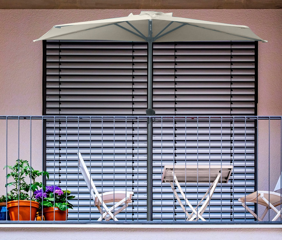 Ein Balkon mit einem grauen, halbrunden Leco Balkon-Sonnenschirm, einem Tisch, zwei Stühlen und Topfpflanzen.