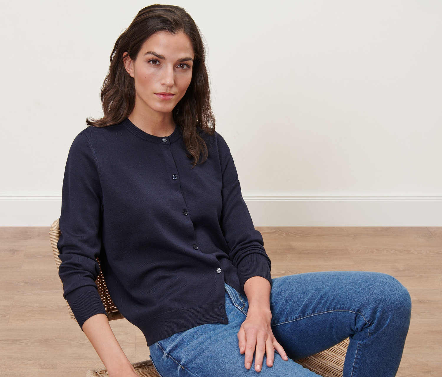 Frau sitzt auf einem Stuhl und trägt einen marineblauen Feinstrick-Cardigan.