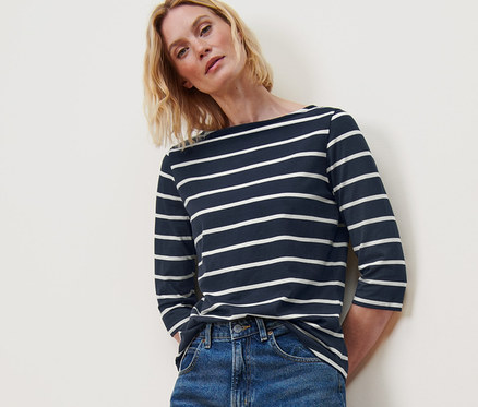 Frau posiert in gestreiftem Shirt mit 3/4-Arm, blauen Jeans und weißen Turnschuhen.