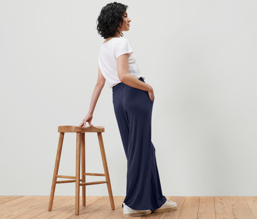 Eine Frau lehnt an einem Hocker und posiert in dunkelblauer Palazzohose.