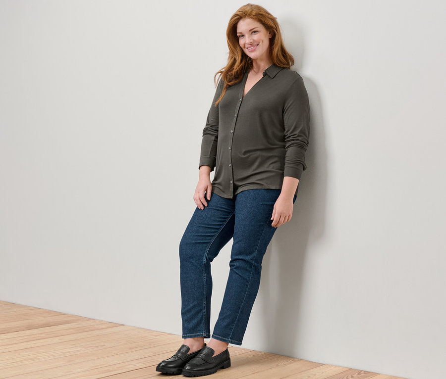 Eine Frau lehnt an einer Wand und trägt ein Blusenshirt mit Knopfleiste und Straight Jeans – Fit »Juna«.