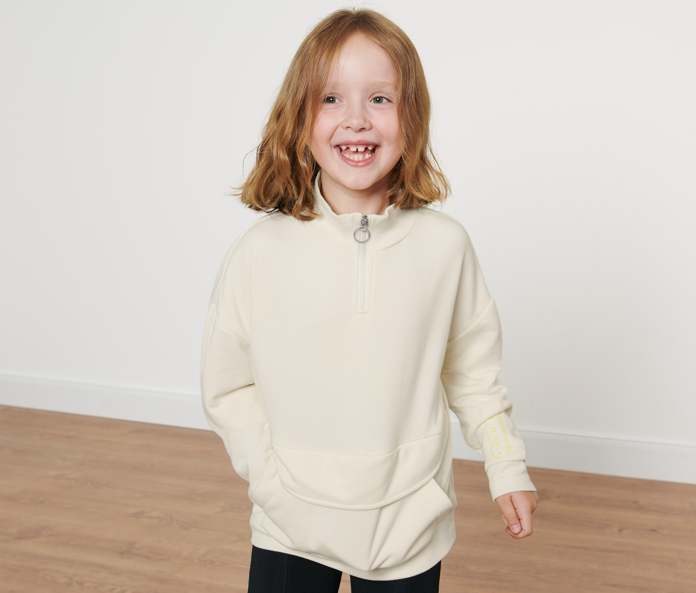 Lächelndes Mädchen posiert in einem cremefarbenen Kinder-Troyer.