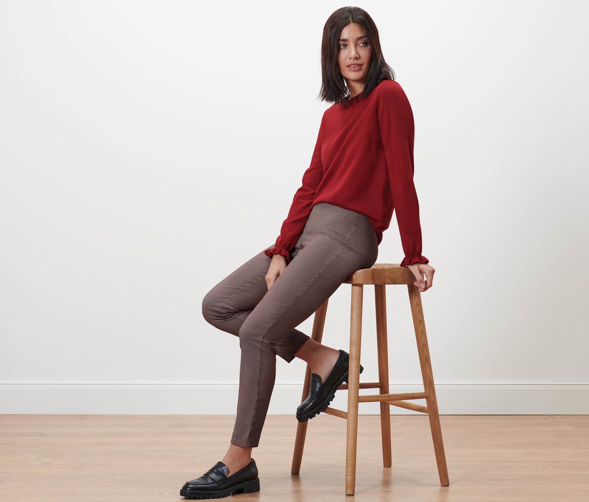 Frau sitzt auf einem Hocker und trägt eine karierte Stretchhose.