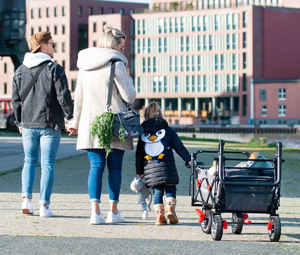 Eine Familie geht und zieht einen Pinolino Klappbollerwagen »Add Plus« auf dem Gehweg.