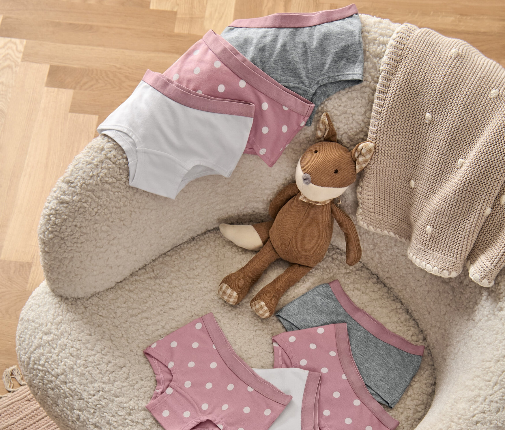 Auf einem Sessel liegen 7 Mädchen-Pantys, ein Plüschfuchs und eine Strickdecke.