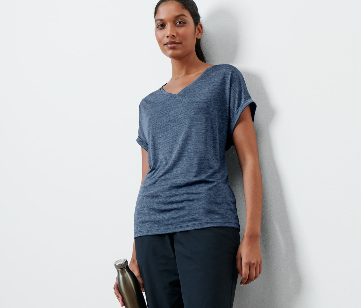 Frau posiert in einem dunkelblauen Funktionsshirt und hält eine Wasserflasche.