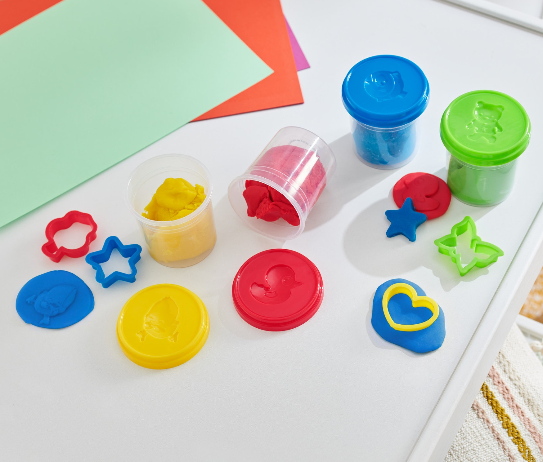 Knete-Set auf einem weißen Tisch mit bunten Papieren.