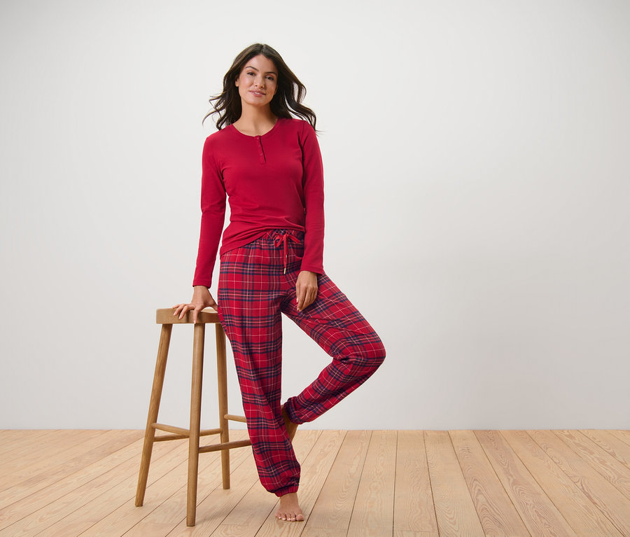 Frau posiert in rot kariertem Flanell-Pyjama, eine Hand auf einem Holzhocker.