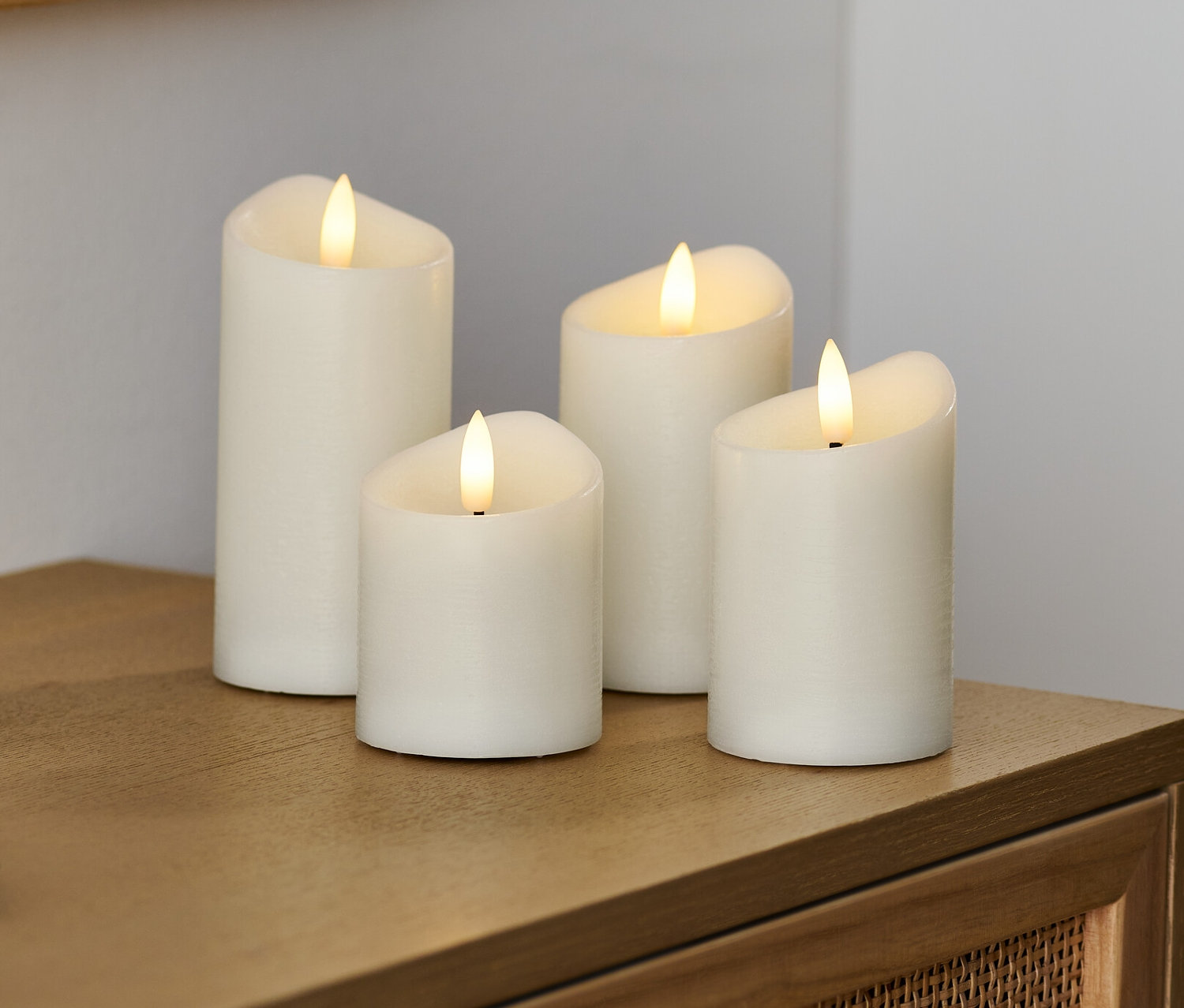 Vier creme LED-Echtwachskerzen stehen auf einer Holzkommode.