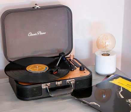 Ein schwarzer Lenco TT-116 Plattenspieler spielt eine Schallplatte neben einer Lampe und Schallplatten.