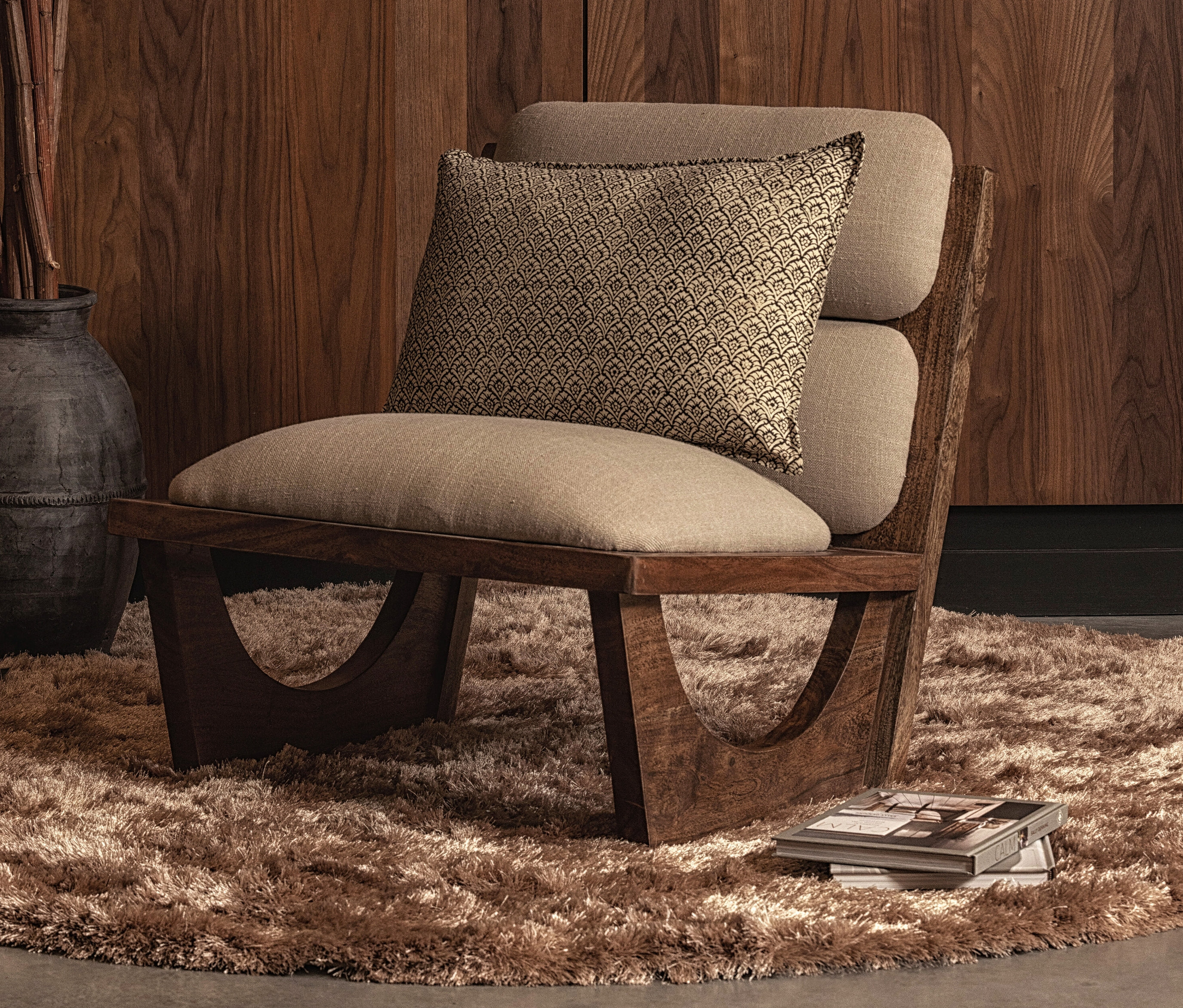 Ein brauner Sessel mit Kissen steht auf dem Woood Teppich »Praline« 200 cm, Nougat.