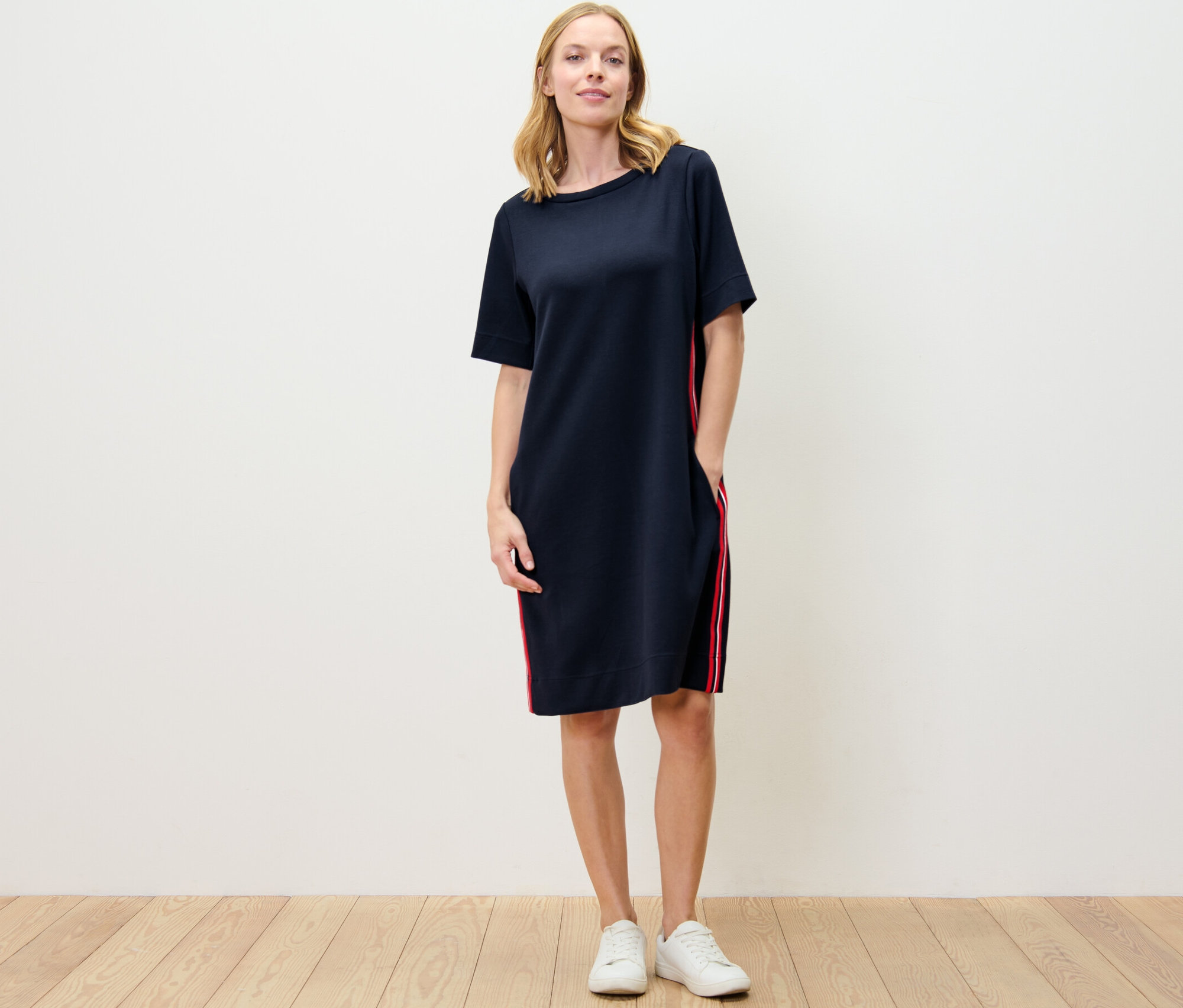 Eine Frau steht und trägt ein Sweatkleid mit Galonstreifen.