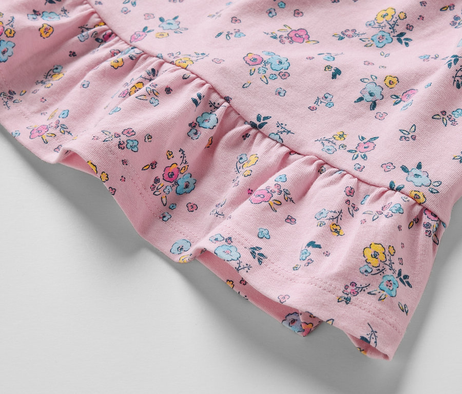 Detailaufnahme eines rosa Baby-Jerseykleids mit Blumenmuster und Rüschen.