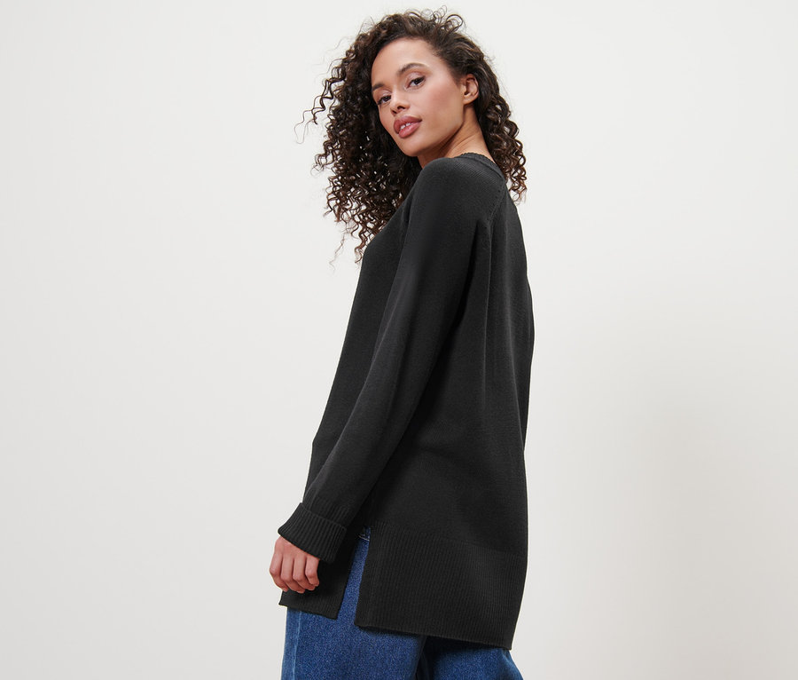 Frau blickt über die Schulter und trägt einen langen schwarzen Strickpullover und Jeans.