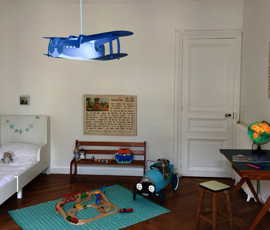 Kinderzimmer mit Holzeisenbahn auf einem blaugrünen Teppich, einem blauen Spielzeugauto und einer blauen »Deckenleuchte »Flugzeug«« als Deckenleuchte.