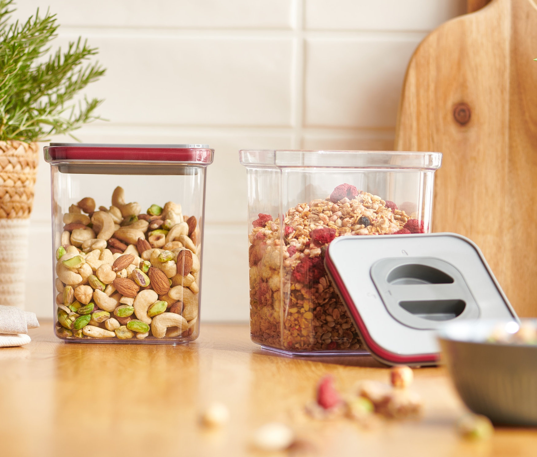 Zwei Vakuum-Frischhaltedosen, eine mit Nüssen, die andere mit Müsli, stehen auf einer Holzplatte.