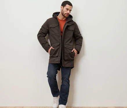 Mann lehnt an einer Wand und trägt eine Parka.
