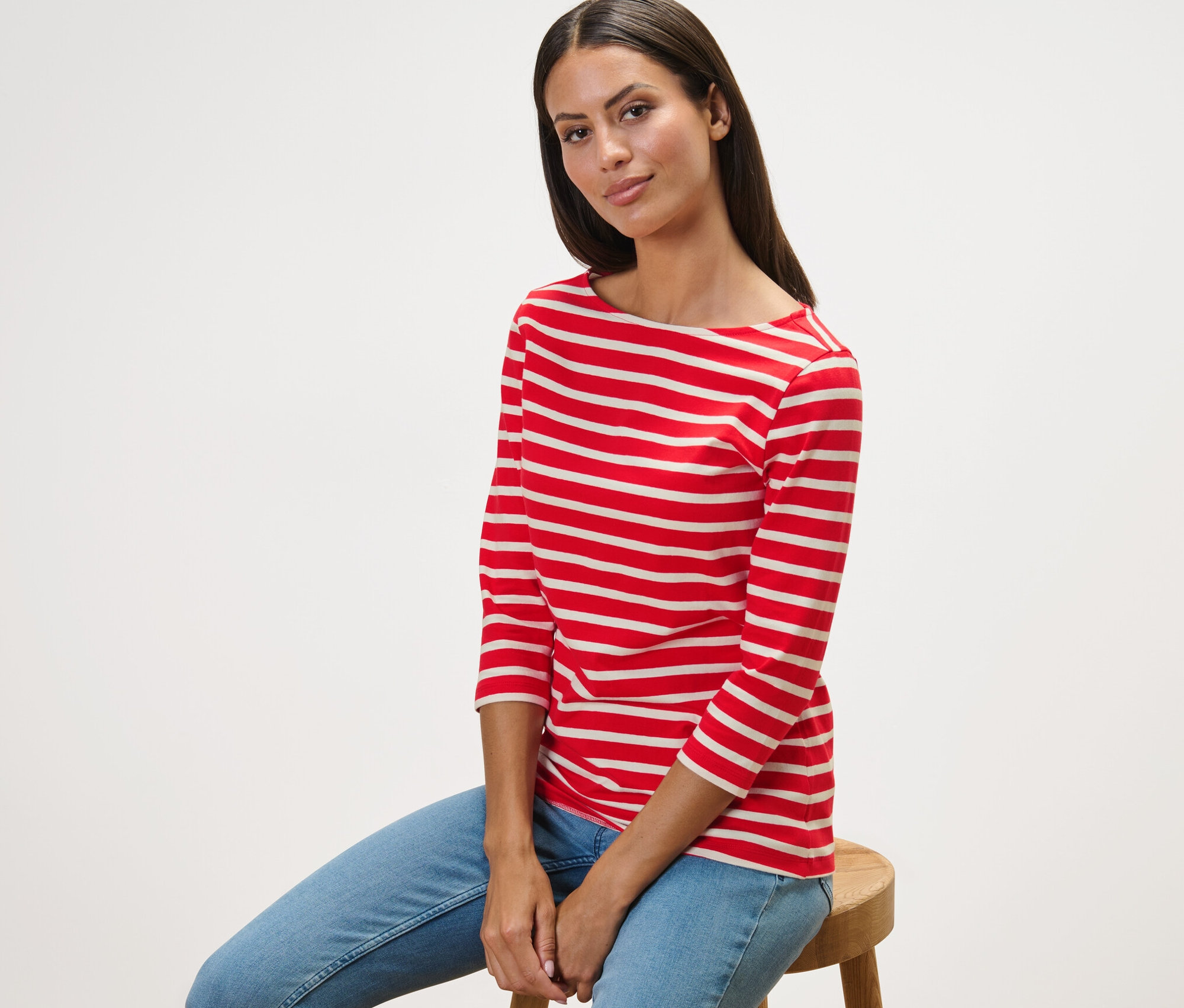 Frau sitzt auf einem Hocker und trägt ein gestreiftes Shirt mit 3/4-Arm, rot getreift.