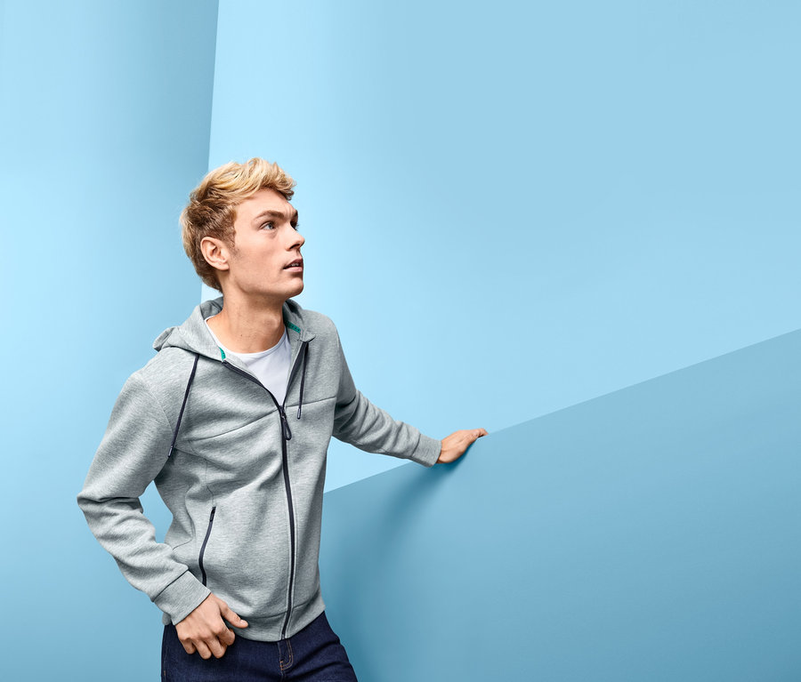 Mann mit blonden Haaren trägt eine Funktions-Sweatjacke und dunkelblaue Jeans.